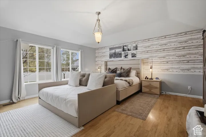 Vaulted ceiling featuring a central pendant light fixture, wood-finish flooring, and horizontal plank accent wall