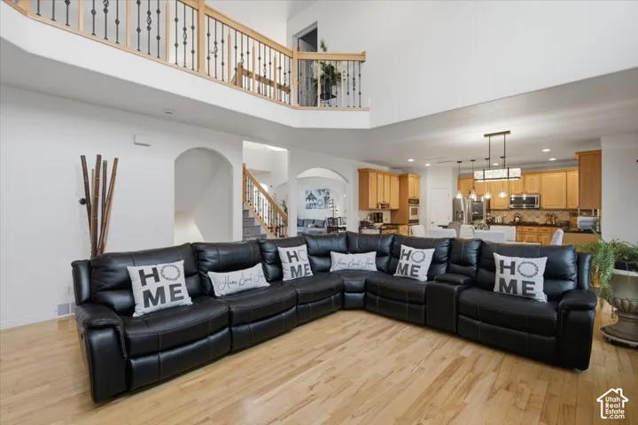 High-ceiling living area featuring wood-finish flooring, an arched entryway, and a balcony with wood and iron railings