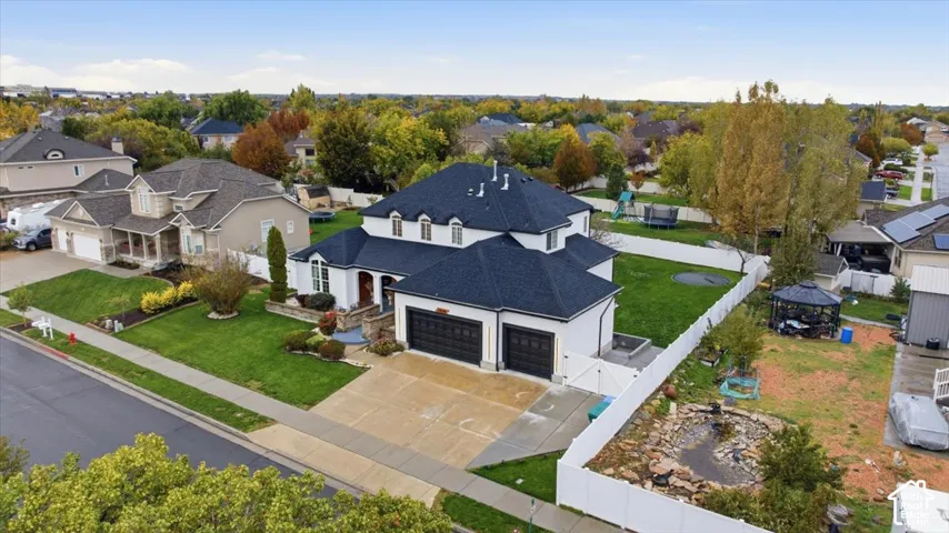Two-story residence featuring a dark shingle roof, stone veneer accents, an attached three-car garage, white vinyl fencing, and an expansive lawn