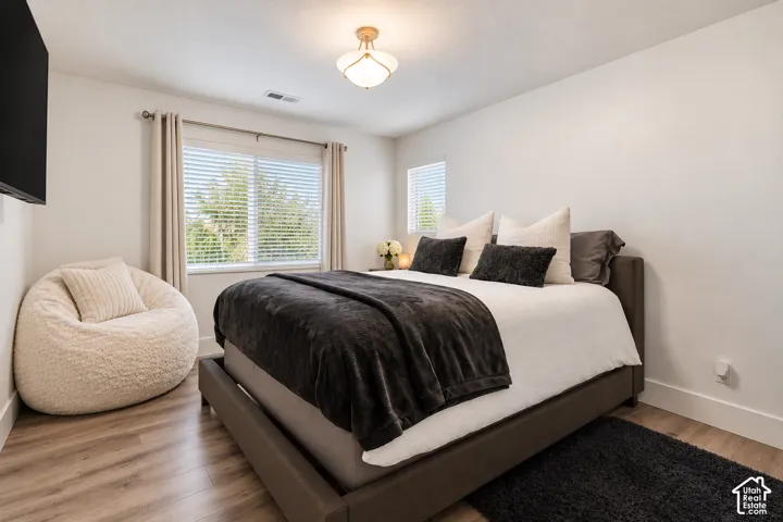 Neutral-toned bedroom featuring wood-finish flooring, dual windows with horizontal blinds, and a semi-flush mount light fixture