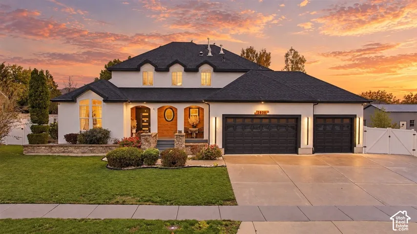 Two-story residence featuring a smooth stucco exterior, multi-gabled roofline, stone-accented entryway, three-car garage, and manicured front lawn