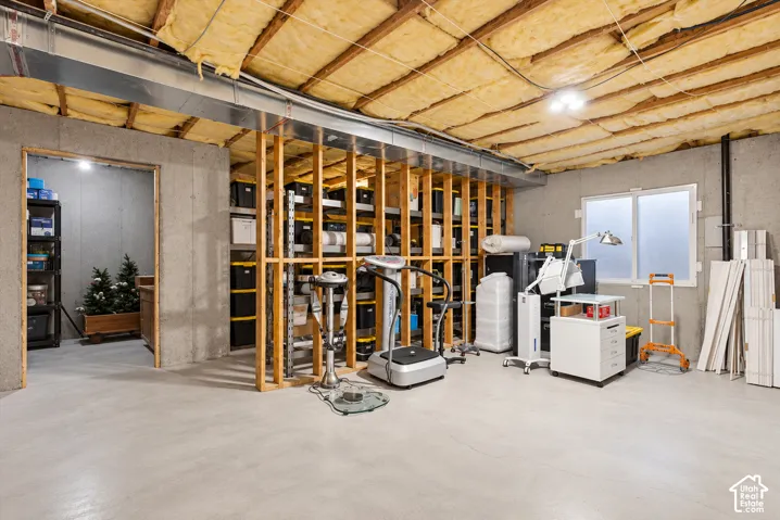 Unfinished space featuring exposed timber framing, concrete foundation walls, painted concrete flooring, an operable sliding window, and fiberglass batt insulation