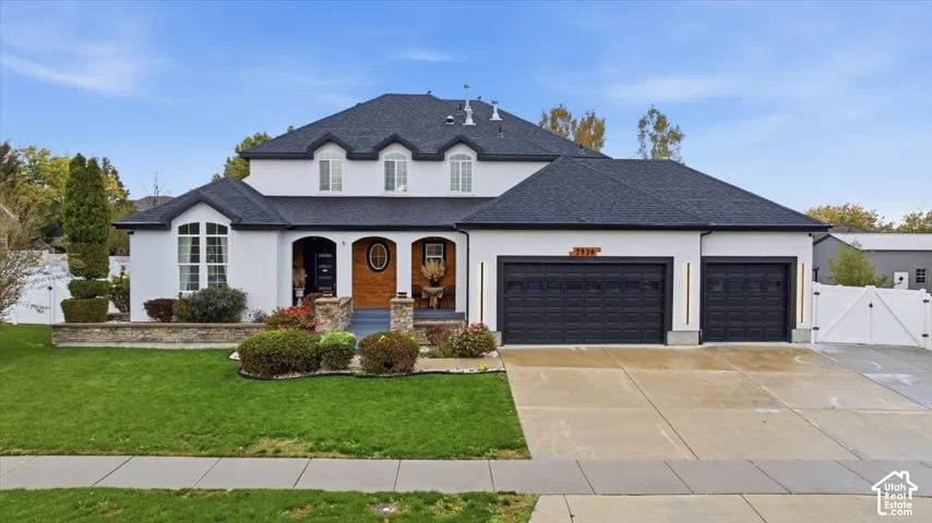 Stucco exterior residence featuring a multi-gabled roof, three-car garage, covered arched porch with stone accents, and manicured front lawn