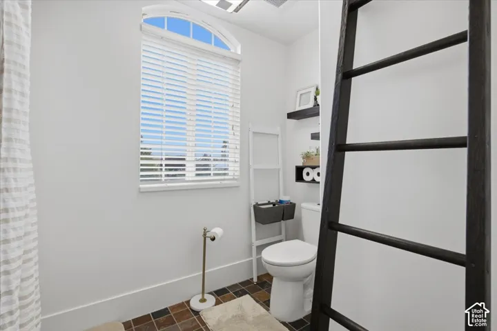 Bathroom featuring an arched window, multi-toned square floor tiling, and a wall-mounted shelving unit