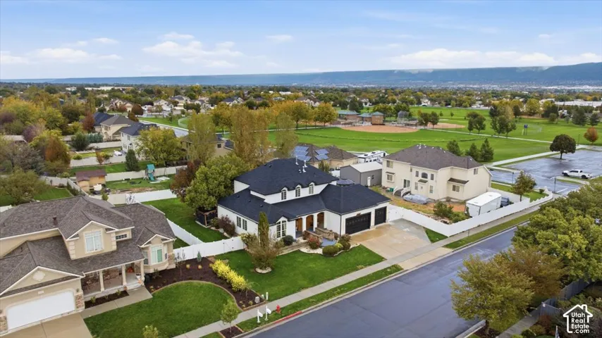 Aerial view of a multi-level residence featuring a dark shingle roof, integrated multi-car garage, white vinyl fencing, and manicured lawns
