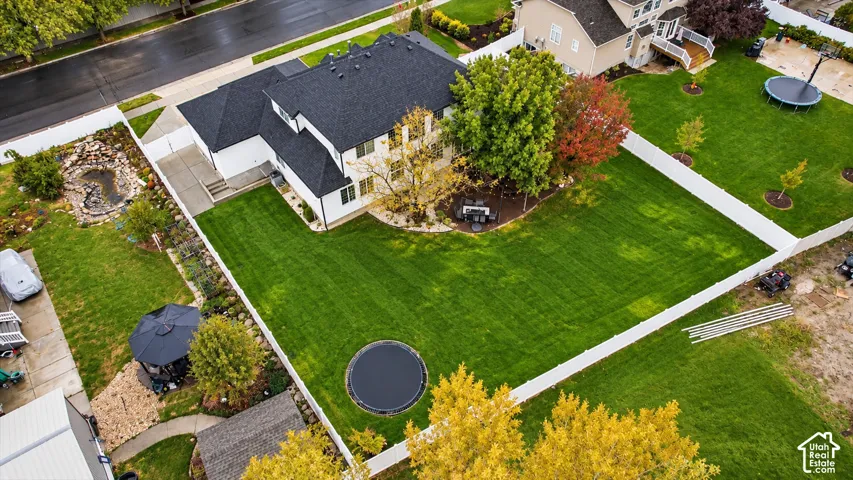 Fenced backyard featuring a manicured lawn, a built-in pond, and mature trees