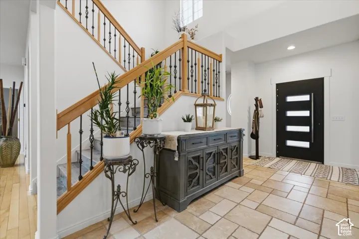 Foyer featuring high ceilings, natural stone flooring in a pattern tile layout, and a staircase with light wood handrails and wrought iron balusters, accented by a dark-finish entry door with horizontal glass panels