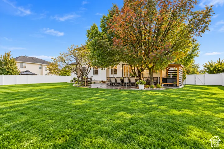 Expansive backyard featuring a manicured lawn, stone patio, custom pergola, and full-perimeter vinyl fencing