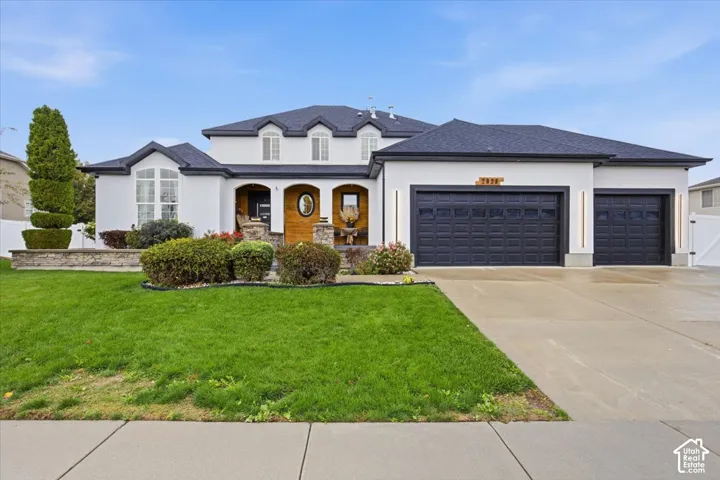 Exterior facade featuring crisp white stucco, stone veneer accents, multi-gabled dark roofing, a recessed covered entryway, and a three-car garage