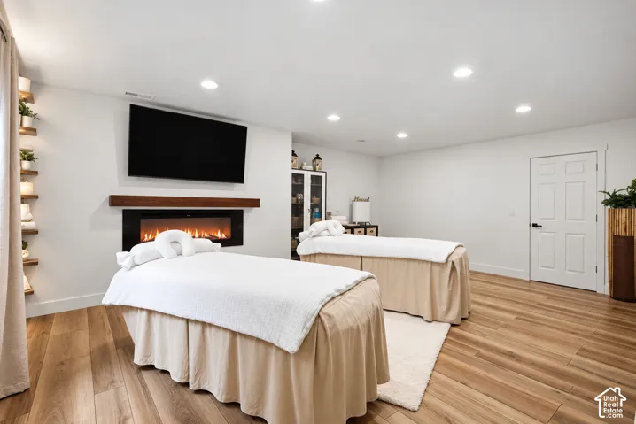 Wall-mounted electric fireplace with a wood-finish mantel, wood-finish flooring, recessed lighting, and built-in wall shelving