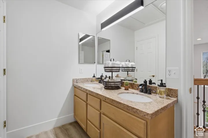 Dual-sink vanity with stone-finish countertop, undermount sinks, matte black widespread faucets, wood-finish cabinetry, and a full-width mirror with integrated linear lighting
