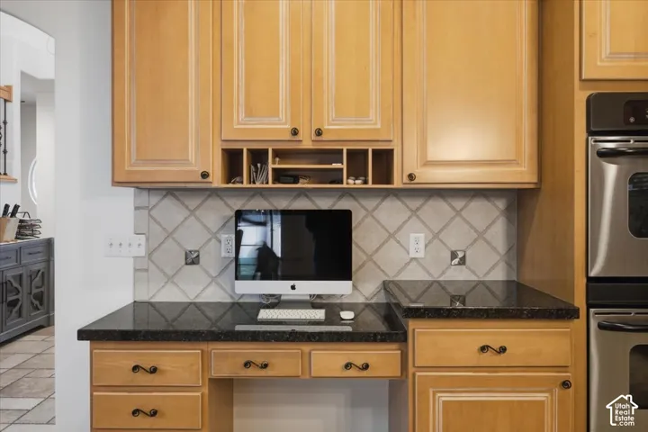 Built-in workspace featuring wood cabinetry, natural stone countertops, a tiled backsplash in a diamond pattern, open shelving, and a stainless steel wall-mounted oven