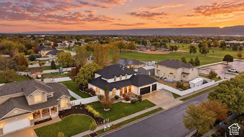 Aerial perspective featuring a multi-story residence with a dark shingle roof, attached multi-car garage, and fenced private grounds