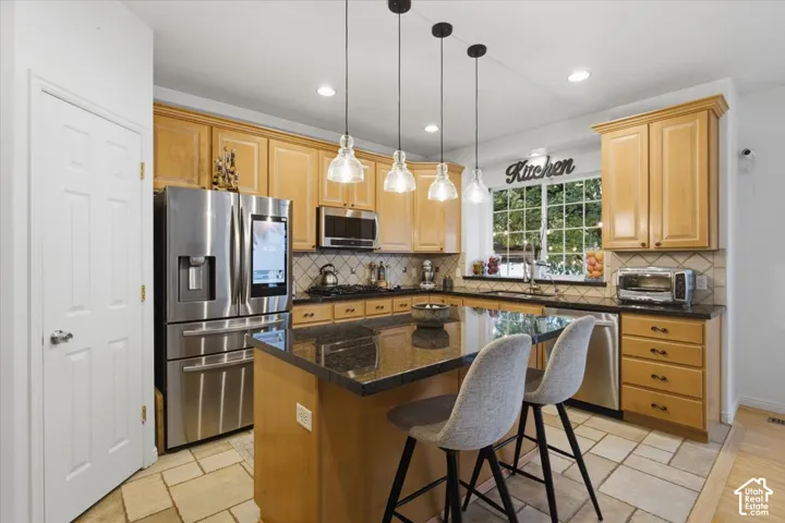 Kitchen featuring light-finish cabinetry, dark stone countertops, stainless steel appliances, stone tile flooring, and a center island with pendant lighting