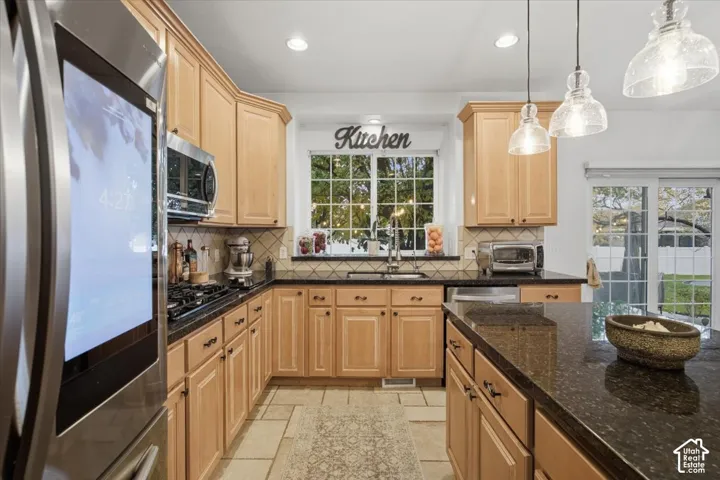 Kitchen featuring light-tone wood cabinetry, dark stone countertops, natural stone tile flooring, stainless steel smart refrigerator, and three pendant lights