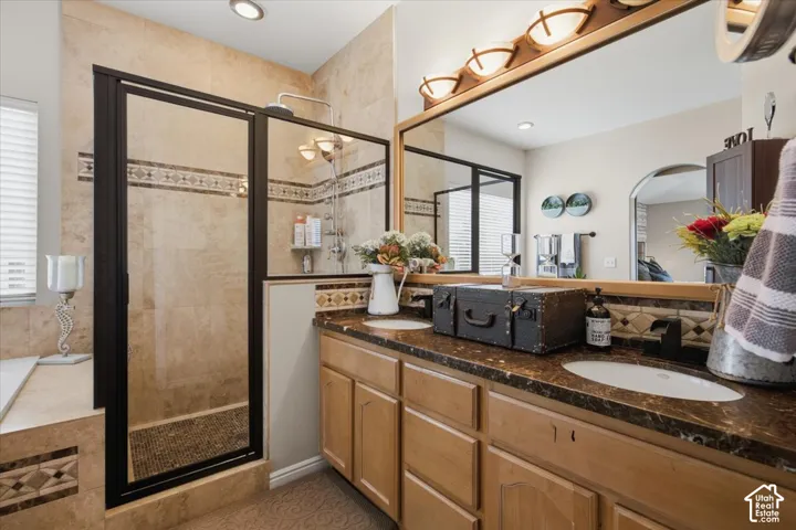 Dual-sink vanity with stone countertop, wood cabinetry, stone-tiled shower with black-framed enclosure, and expansive wall mirror
