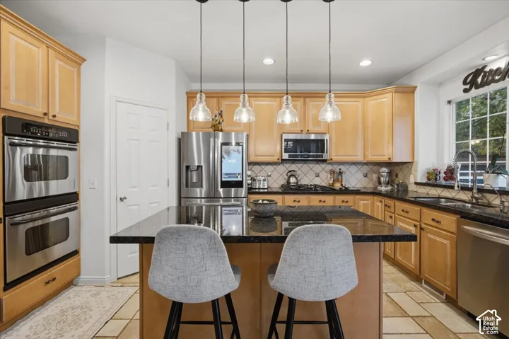 Kitchen featuring natural wood cabinetry, polished stone countertops, stainless steel appliances, a central island, and four glass pendant lights