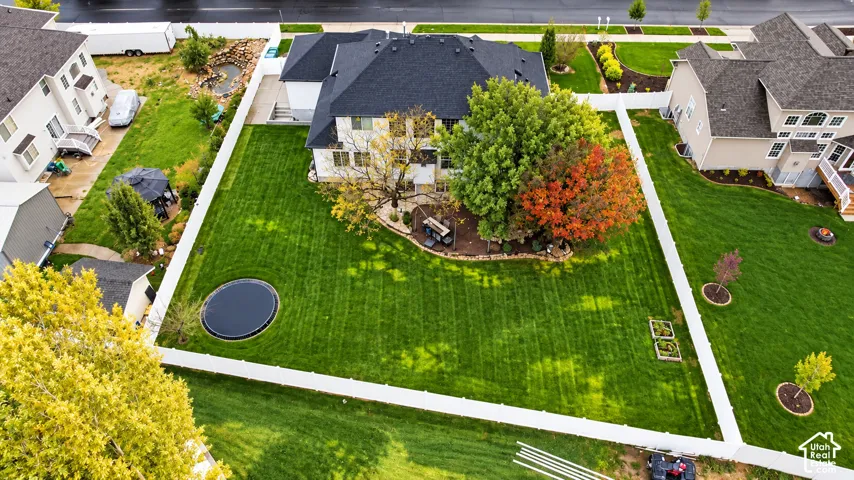 Expansive fenced backyard featuring a manicured lawn, mature trees, tiered stone landscape beds, and a subterranean trampoline