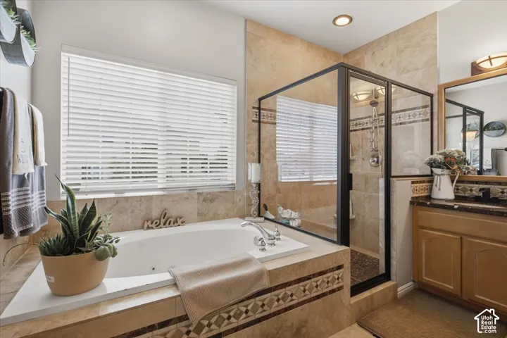 Jetted soaking tub, walk-in shower with a glass enclosure, stone tile surround with decorative accent inlay, and wooden cabinetry with a stone countertop