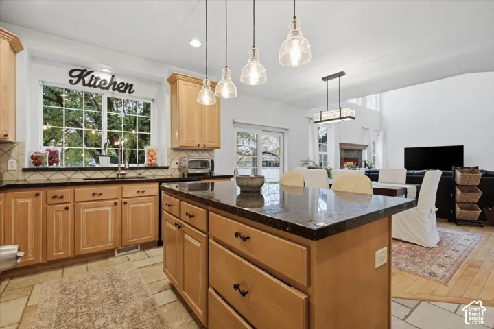 Kitchen featuring natural wood cabinetry, a central island with a stone countertop, tile flooring, pendant lighting, and a window over the sink