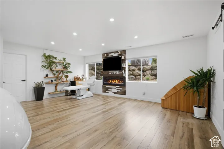 Wood-finish flooring, recessed lighting, and a linear electric fireplace featuring a decorative stone and wood-slat accent wall