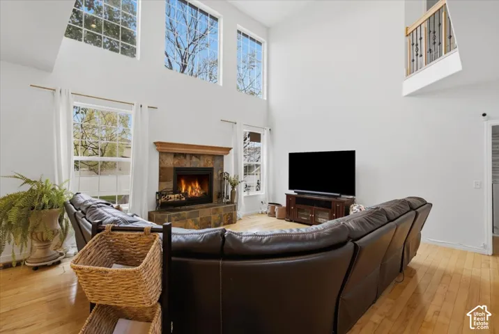 Two-story living area featuring floor-to-ceiling windows, natural wood-finish flooring, and a stone-surround fireplace with a wood mantel