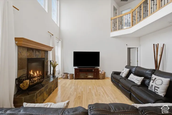 Living room featuring a double-height ceiling, wood-finish flooring, and a fireplace with a stone-surround hearth and wooden mantel, complemented by an overlook with a wood and metal railing