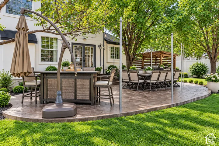 Stamped concrete patio with a wooden pergola, mature trees, and landscape lighting