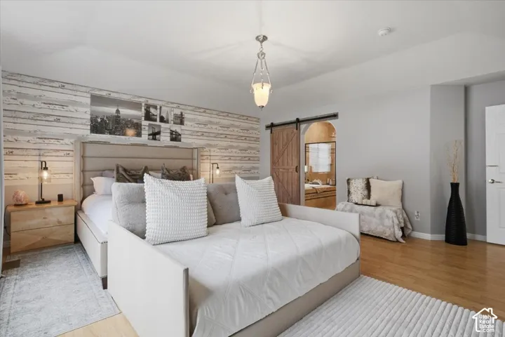 Vaulted ceiling with a central pendant light, wood-finish flooring, accent wall with horizontal planks, and a sliding wood barn door