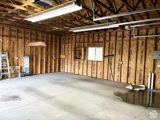 Garage featuring exposed stud walls, concrete flooring, dual overhead fluorescent light fixtures, and a single-pane window