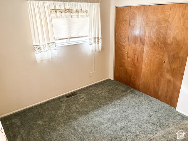 Room featuring wall-to-wall carpeting, wood-finish bi-fold closet doors, and a window with horizontal blinds