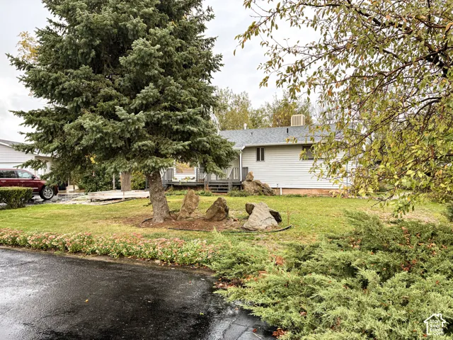 Exterior featuring horizontal siding, a raised deck, mature evergreen landscaping, decorative boulder rock formations, and perennial garden beds