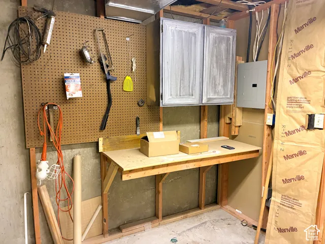 Built-in wooden workbench, wall-mounted pegboard organization system, overhead cabinetry, electrical service panel, and exposed wall framing