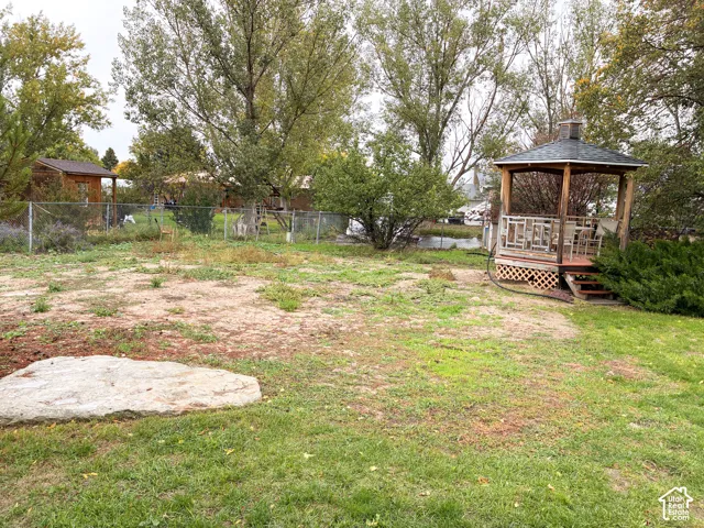Backyard featuring a wooden gazebo with latticework base, mature trees, chain-link fencing, and a large natural stone boulder