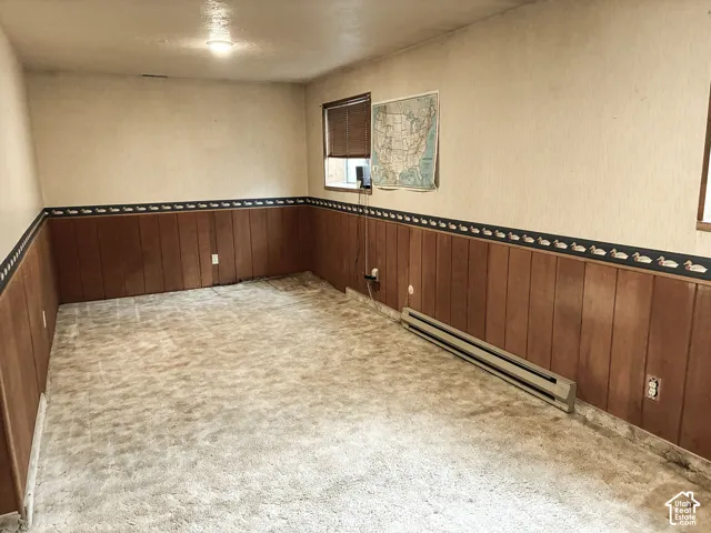 Interior space featuring wood-paneled wainscoting with decorative border, window with blinds, and carpeting
