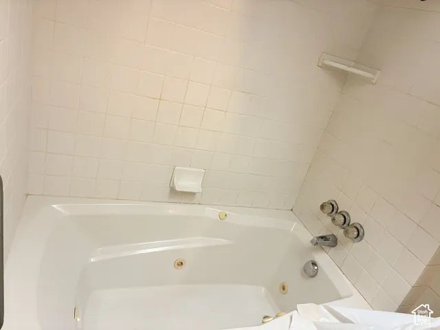 Jetted soaking tub featuring white ceramic wall tile, integrated soap dishes, and metallic three-handle plumbing fixtures