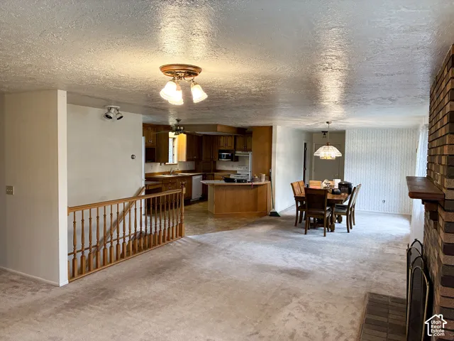 Open-concept interior featuring a floor-to-ceiling brick fireplace, wood-finish cabinetry, a breakfast bar, and a wooden stair railing