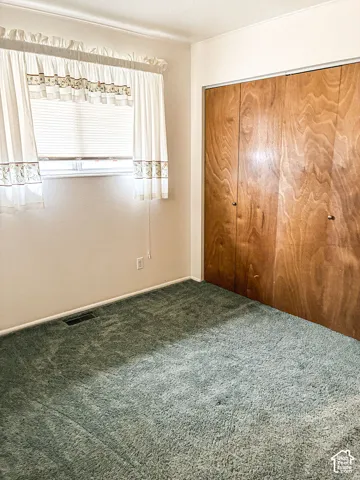 Room featuring wall-to-wall carpeting, wood-finish closet doors, and a window with horizontal blinds