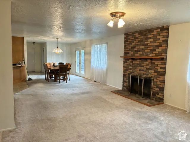 Floor-to-ceiling brick fireplace with a wooden mantel and integrated metal screen, carpeted flooring, and dual glass-paned doors