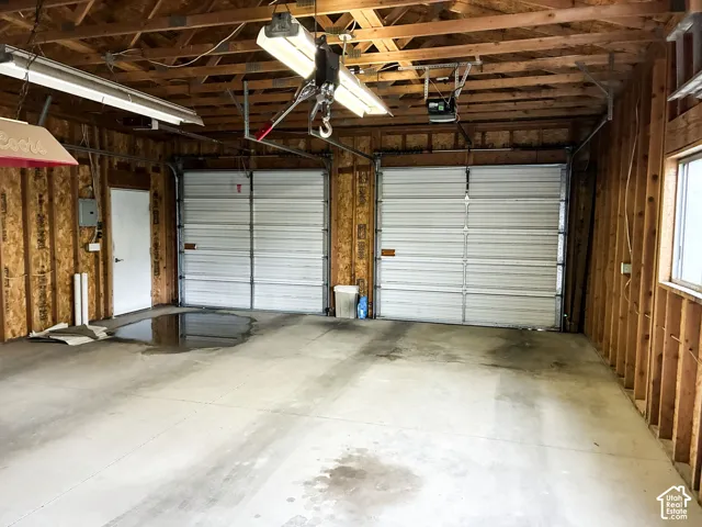 Two-car garage featuring exposed wood framing, concrete flooring, two metal sectional doors, and overhead fluorescent lighting