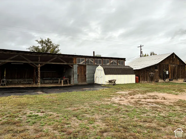 Expansive acreage featuring dual wood-sided barn structures, a covered outdoor work area, and a standalone storage shed with asphalt shingling