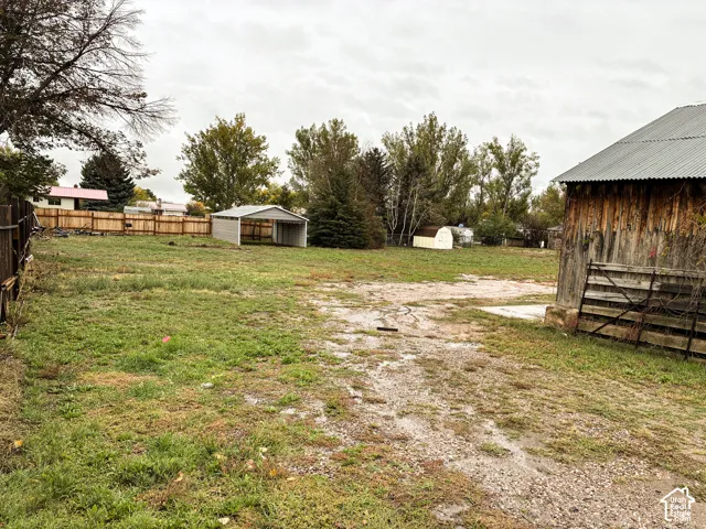 Expansive lot featuring a metal-sided barn, detached carport, perimeter wooden fencing, and mature trees