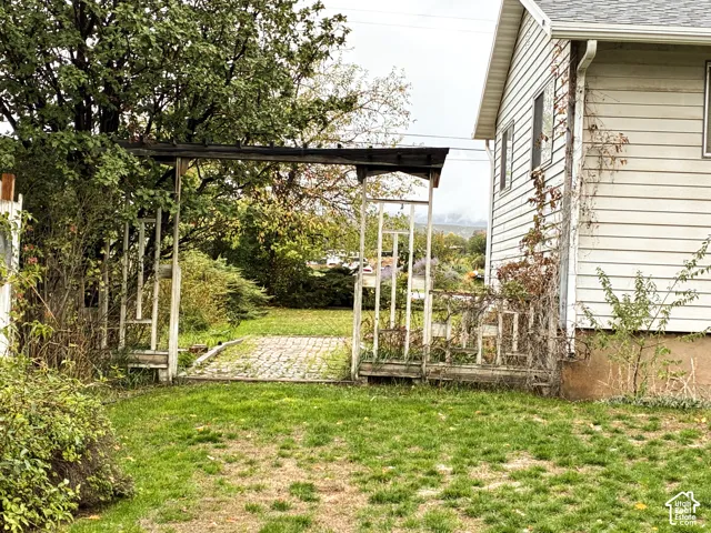 Exterior side yard featuring a brick-paved path, a custom wood trellis structure, and horizontal lap siding