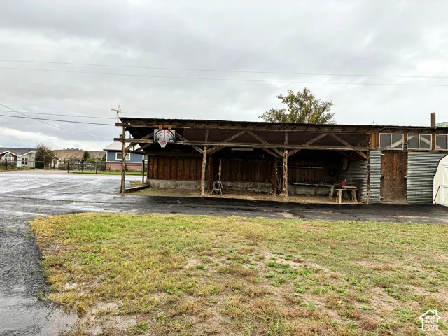 Open-air timber frame structure featuring wood siding, metal roofing, concrete foundation, and paved surface