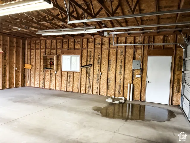 Spacious garage interior featuring exposed wood-stud walls, a concrete floor, integrated ceiling-mounted lighting, a single-pane window, and an exterior side-access door