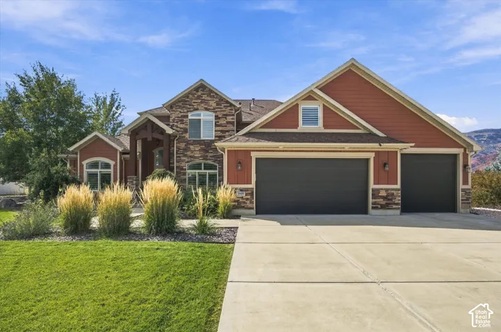 Multi-gabled exterior featuring horizontal siding, natural stone veneer accents, an arched covered entryway, and a three-car garage