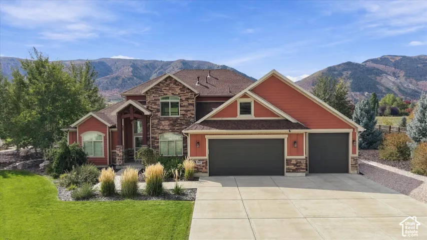Multi-gabled exterior featuring stone masonry accents, horizontal siding, an attached three-car garage, and concrete driveway, set against a mountain backdrop