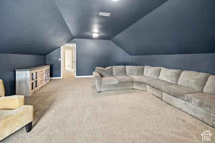 Expansive room featuring vaulted ceilings, carpeted flooring, and a built-in cabinet with a stone countertop