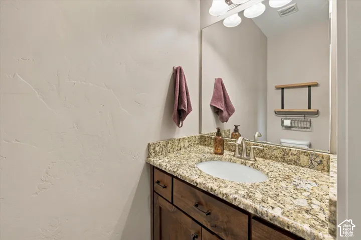 Stone countertop with integrated oval sink, dark wood-finish cabinetry, full-width vanity mirror, and multi-bulb light fixture