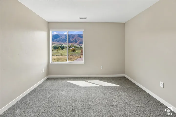 Neutral interior room featuring neutral wall paint, textured wall-to-wall carpeting, and a large window showcasing a mountain landscape